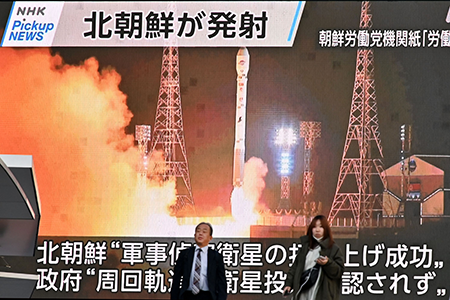 Pedestrians walk past a video screen in Tokyo displaying the launch of North Korea's reconnaissance satellite 'Malligyong-1' on November 22, 2023. (Photo by Kazuhiro Nogi/AFP via Getty Images)